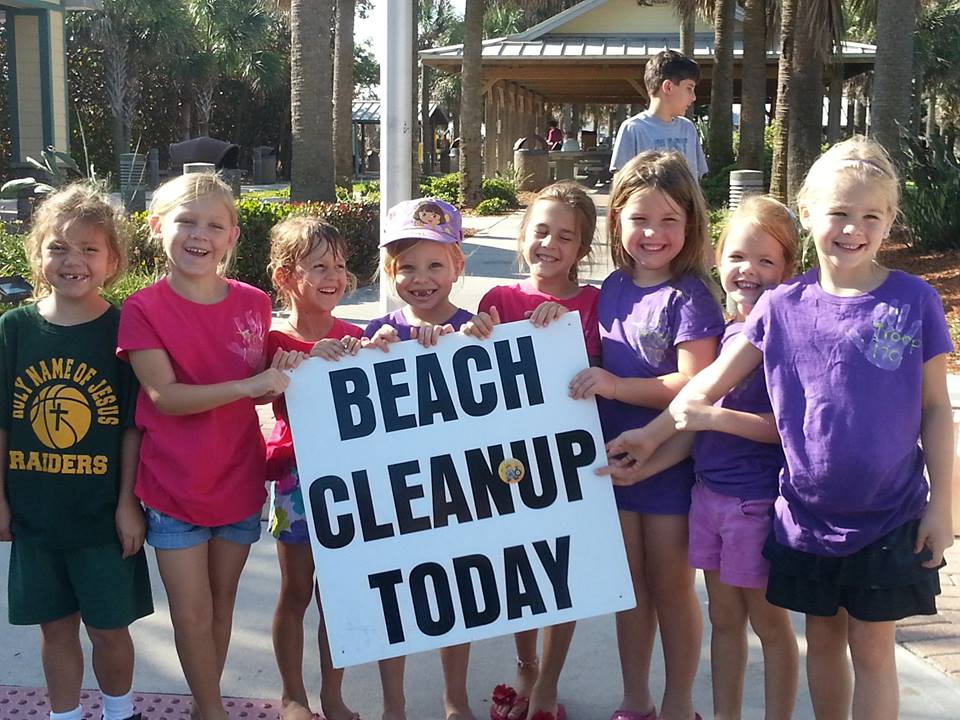 7 young girls from the daisies, troop 170 smiling at the camera, holding a "Beach Cleanup" sign